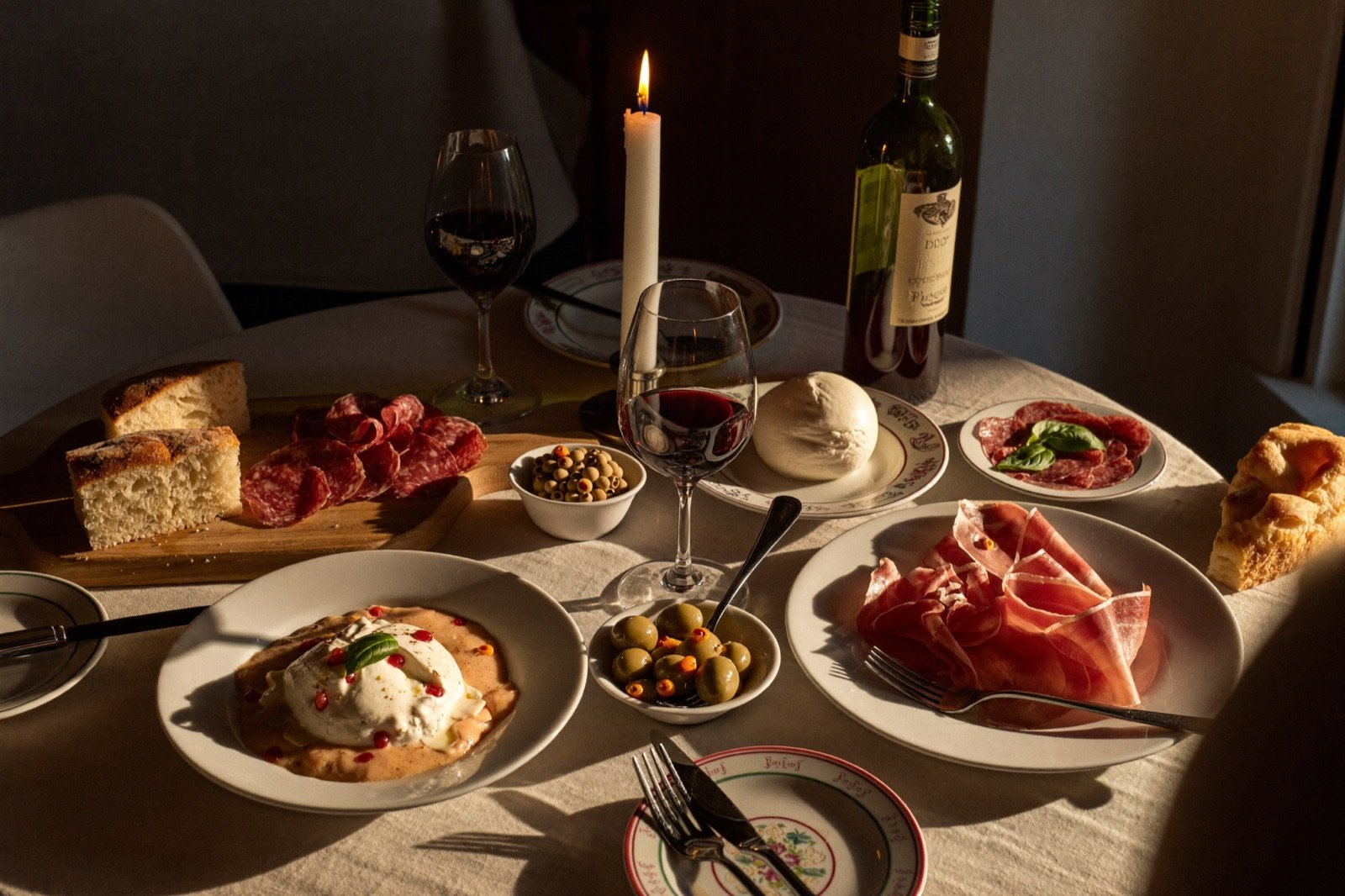 Antipasti-Platte mit Parmaschinken, Burrata, Oliven und Focaccia bei Kerzenlicht